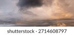 Cloudscape featuring a dramatic sunset sky with thick, dark clouds and warm orange hues over the horizon.