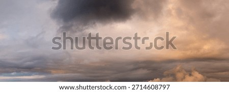 Cloudscape featuring a dramatic sunset sky with thick, dark clouds and warm orange hues over the horizon.