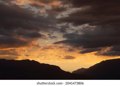 Cloudscape. Magical view of a dramatic sunset in the mountains. The beautiful sky, clouds and mountain dark silhouette with dusk colors.