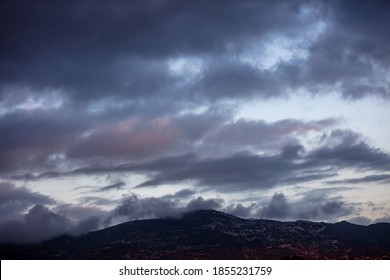 Cloudscape at sunset. Heavy dark clouds on sky over mountains background. Sunbeams through fluffy clouds color the blue sky and the hills black silhouette.