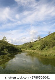 Cloudy blue sky reflected in a pond on MiIlington Beck which is in the Yorkshire Wolds