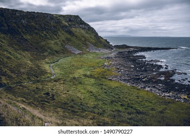 A Cloudy Day At The Cliffs Of Giant's Causeway With People Hiking At The Footpath. 