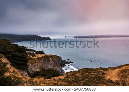 Cloudy day on the Pacific Ocean coastline; Golden Gate bridge covered by fog visible in the background; Marin Headlands, North San Francisco Bay Area, California