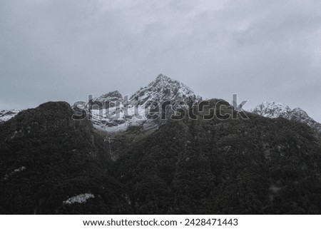 Cloudy moody stormy gray sky and cold snow capped glacier textured mountain peak in natural New Zealand tourism national park landscape scenic view