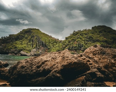 Cloudy and overcast atmosphere on the edge of the beach with rocks and green hills on the edge
