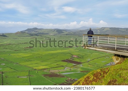 Cloudy sky, Achada Plain valley, agricultural fields and pastures, mountainous landscape and volcanic craters, viewpoint Serra do Cume and man standing on the bridge. Terceira Island, Azores, Portugal