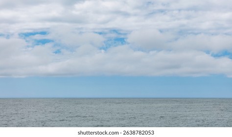 A cloudy sky with a blue sky in the background. The sky is mostly cloudy with a few white clouds scattered throughout. The ocean is calm and the water is a deep blue color