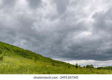 A cloudy sky with a hill in the background. The sky is overcast and the grass is green - Powered by Shutterstock