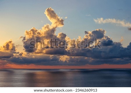 A cloudy sky over a calm body of water. The clouds are a variety of shapes and sizes, and they are casting shadows on the water. The water is a deep blue color, and it is reflecting the clouds.