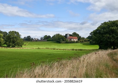 The cloudy sky over the field and old chapel with a weathervane on top of its tower
