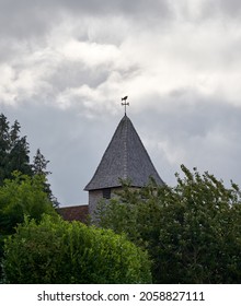 The cloudy sky over the old building with a weathervane on top of its tower