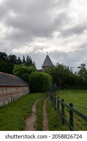 The cloudy sky over the road leading to old building with a weathervane on top of its tower