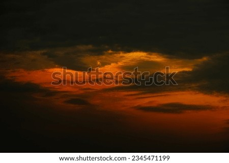 A cloudy sky with a sunset in the background. The sun is setting behind the clouds, creating a beautiful and colorful display.