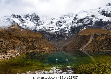 Cloudy snow capped mountain with reflection at the high altitude emerald green glacial Laguna Humantay lake, Cusco - Powered by Shutterstock