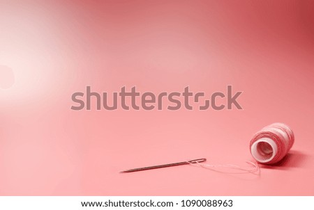 Clouse up pink spool of thread and needle on a pink background. Copy space
