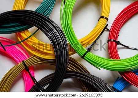 Clouse-up view of multiple coils of 3D printer filament in various vibrant colors, neatly arranged on a white surface.