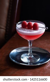 Clover Club Cocktail with Gin, Lemon Juice, Raspberries, and Egg White Foam in a Glass in a Dark Luxurious Bar