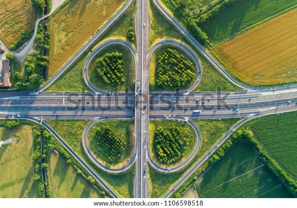 Cloverleaf interchange seen from above. Aerial view\
of highway road junction in the countryside with trees and\
cultivated fields. Bird\'s eye\
view.
