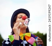 Clown blowing bubbles at outdoor festival for fun, fantasy and summer adventure in nature. Face of person, street performer or circus character in park with creative color at happy carnival event.