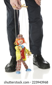 A clown marionette performing between the legs and under the hand of a puppet master.  Isolated on white.