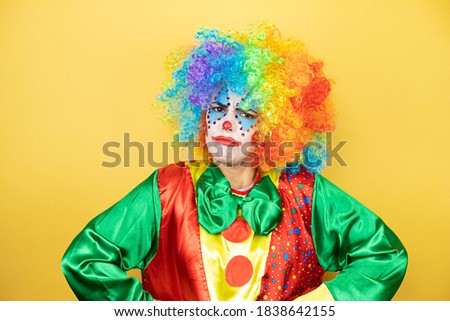 Clown standing over yellow insolated yellow background skeptic and nervous, disapproving expression on face with arms in waist