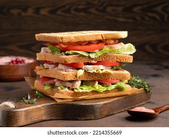 Club sandwich close up view. Delicious layered sandwich with toasted bread, turkey (grilled chicken), tomatoes slices, salad leaves, bacon, thyme and aoili cranberry sauce. Brown wooden background. - Powered by Shutterstock