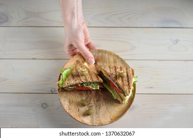 Club sandwich with ham and cheese on a wooden plate. Plate with sandwiches in a female hand. Light wooden background. View from above. - Powered by Shutterstock