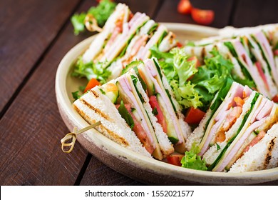 Club sandwich with ham, tomato, cucumber, cheese,  and arugula on wooden background. - Shutterstock ID 1552021577