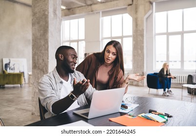 Clueless Multiracial Colleagues In Casual Clothes Shrugging Shoulders And Looking At Computer Screen While Working On Business Strategy In Spacious Office