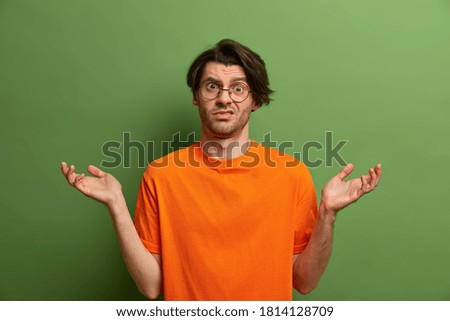 Clueless uncertain doubtful adult man spreads palms sideways and has no clue what happening or how to act. Puzzled unaware guy in bright clothes cannot decide what to do, spreads hands sideways.