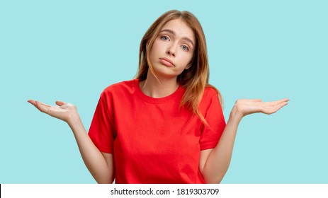 Clueless woman portrait. Whatever gesture. Indifferent lady in red t-shirt shrugging isolated on blue background. No idea. Who cares. Fail sorry.