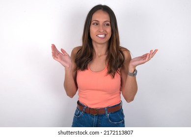 Clueless young beautiful caucasian woman wearing orange top over white background shrugs shoulders with hesitation, faces doubtful situation, spreads palms, Hard decision