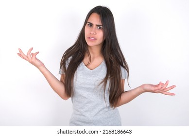 Clueless young caucasian woman wearing grey t-shirt over white background shrugs shoulders with hesitation, faces doubtful situation, spreads palms, Hard decision