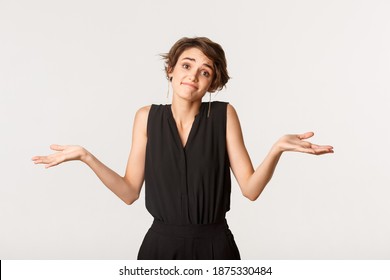 Clueless Young Woman Apologizing For Being Unaware, Shrugging With Awkward Smile, Standing White Background