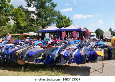 Cluj-Napoca, Romania - August 18, 2019: Many trousers, overalls, working clothes on outdoor tables at the flea market. Dresses and shirts and other clothing is hanging at the stalls in the background.