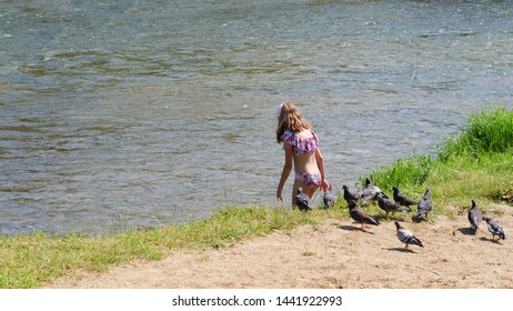 Cluj-Napoca, Romania - July 3, 2019: Young girl in bathing suit enters the river to cool herself down on a hot summer day
