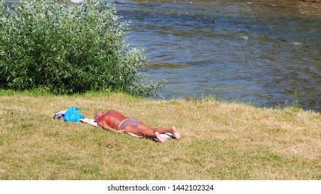 Cluj-Napoca, Romania - July 3, 2019: Elderly sun tanned man basks in the sun on the river bank