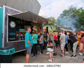 Cluj-Napoca, Romania - May 5, 2018: People Stay In Line To Buy Fast Food At Food Trucks In The Evening. Grill Smoke In The Background.