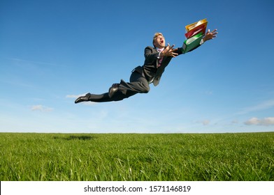 Clumsy Businessman Tripping Dramatically With His File Folders Outdoors In A Green Grass Meadow