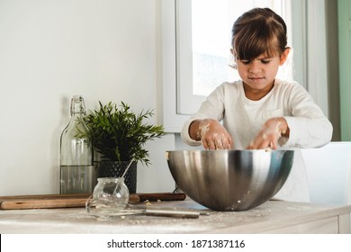 Clumsy Little Cute Girl Is Cooking On Kitchen And Looking Inside The Bowl - Having Fun While Making Pizza, Bread Or Cake Dough - Childhood Concept And Having Fun Cooking - Copy Space For Text On Left