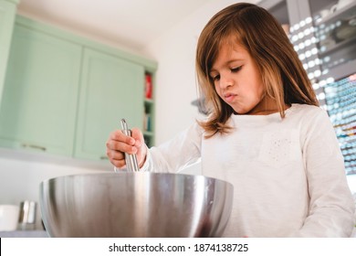 Clumsy Little Cute Girl Is Cooking On Kitchen And Looking Inside The Bowl - Having Fun While Making Pizza, Bread Or Cake Dough - Childhood Concept And Having Fun Cooking - Copy Space For Text On Left