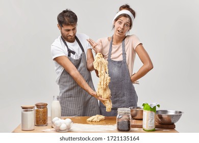 Clumsy Man In Apron Stretches Sticky Dough, Has Difficulties During Cooking, Indignant Housewife Stands Near, Cannot Understand Whats Wrong. Bad Cookers At Kitchen. Culinary Courses For Amateurs