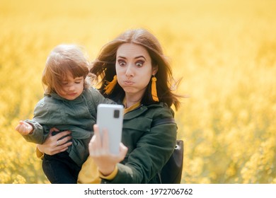 Clumsy Mom And Upset Daughter Taking Selfies In Rapeseed Field. Mother Trying To Take A Mobile Photo With Her Child With Wind Ruing Her Hair
