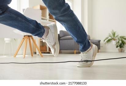 Clumsy Person Falls Down After Stumbling Over A Power Cable. Man Or Woman In Sneakers Trips Over An Electrical Cord While Walking On The Floor At Home. Cropped Shot. Domestic Accident Concept