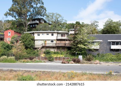 A Cluster Of Houses On A Tree Lined Hill Above A Busy Road