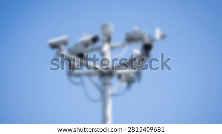 A cluster of security cameras is mounted on a metal pole, pointing in various directions against a bright, cloudless blue sky.