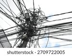 Cluttered bundle of overhead electric power lines and communication cables on the pole. Many electric wires. Utility pole with many cables and street light. Chaotic electric wires 