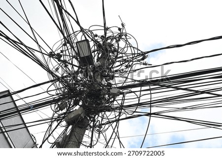 Cluttered bundle of overhead electric power lines and communication cables on the pole. Many electric wires. Utility pole with many cables and street light. Chaotic electric wires 