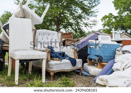 A cluttered collection of household items, including upholstered chairs and a vintage cooler, sits abandoned on a suburban curb, illustrating themes of waste, moving day, or garage clearance.