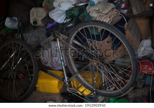 a cluttered garage and an\
old disassembled bicycle without a wheel, mountains of garbage in a\
barn